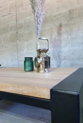 Close-up van een houten tafel gemaakt van eikenhout in een stalen frame. Op de tafel staat een mijnwerkers lamp een groene kaars en een spriet in een vaasje